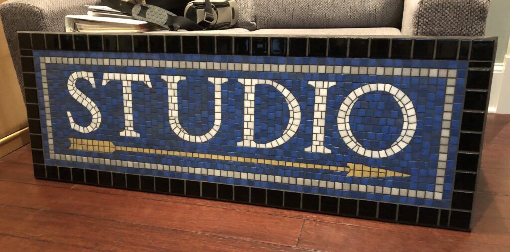 The mosaic tile STUDIO sign leaning against a couch, ready for installation